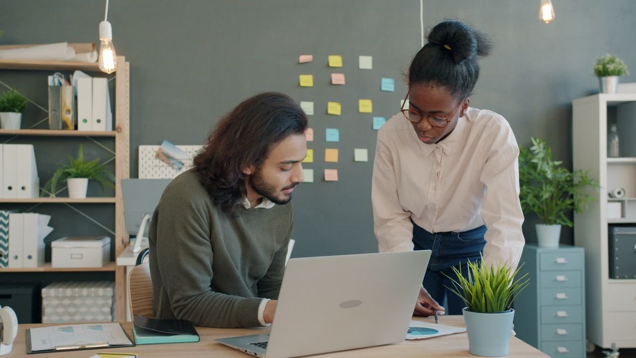 Two colleagues collaborating at a desk with laptop in a modern office space.